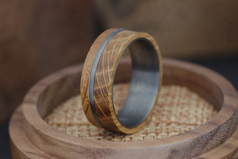 May include: A wooden ring with a silver band. The wood is a light brown colour and has a natural grain pattern. The ring is sitting on a wooden surface.