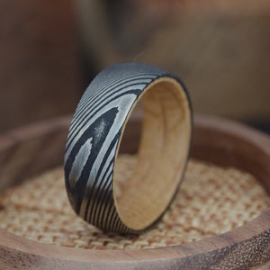 May include: A black and silver patterned ring with a wooden band. The ring is sitting on a wooden surface.