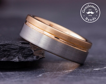 May include: A silver and gold wedding band with a brushed finish. The band has a thin gold inlay.