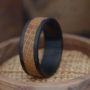 May include: A black and brown wooden ring with a black band around the edge. The ring is sitting on a wooden surface.