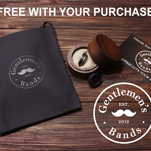 May include: A black velvet pouch with a silver logo that reads "Gentlemen's Bands Est. 2019" and a small silver moustache. The pouch is on a wooden surface with a wooden ring box and a business card that reads "Thank you for your order. Gentlemen's Bands. Appreciate your business."