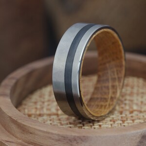 May include: A silver and black ring with a wooden inlay. The ring is sitting on a wooden surface.