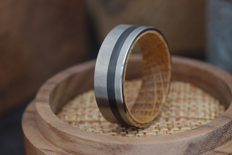 May include: A silver and black ring with a wooden inlay. The ring is sitting on a wooden surface.