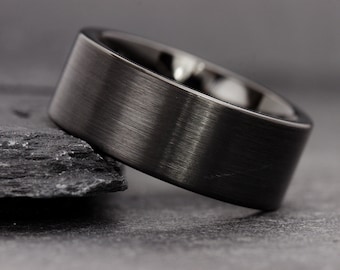 May include: A black brushed metal ring with a wide band.