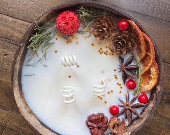 May include: A white candle in a wooden bowl with a variety of decorative elements, including pine cones, dried orange slices, red berries, and gold glitter.