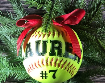 May include: A yellow softball Christmas ornament with a red ribbon and the name "LAUREN #7" printed on it.
