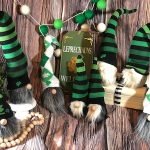 May include: Seven gnomes with green and black striped hats and green and white patterned hats. The gnomes are sitting on a wooden surface with a sign that says "LEPRECHAUNS WELCOME".
