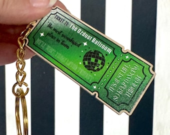 May include: A green and gold keychain in the shape of a ticket. The ticket reads "Ticket to The Ozdust Ballroom" with the text "The most swankified place in town" and "It's just life so keep dancing through".