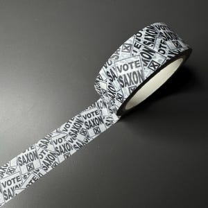 May include: A roll of white washi tape with a repeating pattern of black squares that say "Vote Saxon" in all caps.