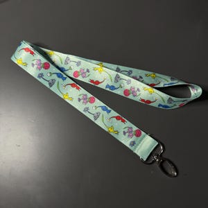 May include: A light blue lanyard with a repeating pattern of colourful cartoon animals and flowers. The lanyard has a silver swivel clasp.