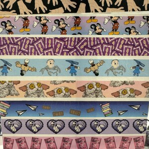 Op de afbeelding: Een verzameling kleurrijke washi-tapes met verschillende ontwerpen, waaronder Mickey Mouse, een paars en geel patroon, een blauw en wit patroon met personages, een beige en wit patroon met dierengezichten, een blauw en wit patroon met papieren vliegtuigjes, een paars en wit patroon met harten en een personage, en een roze en wit patroon met boeken.