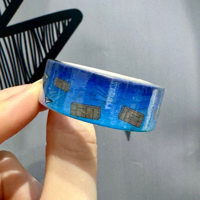 Op de afbeelding: Een rol blauwe washi tape met een verloop en kleine, herhaalde afbeeldingen van bruine dozen.