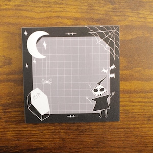May include: Black and white Halloween themed sticky note with a spider web, a crescent moon, a tombstone that says "RIP", a skeleton figure, and bats. The note has a gray grid pattern.