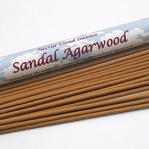 May include: A collection of brown incense sticks with a red cap tube. The tube is labeled "Nectar Cloud Incense Sandal Agarwood" in white and red text against a blue sky and cloud design. The incense sticks are arranged on a white surface.
