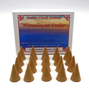 May include: A box of 20 Himalayan Cedar incense cones. The box is white with red and blue text that reads "Nectar Cloud Incense Himalayan Cedar". The cones are brown and arranged in a rectangular pattern on a white surface. Ingredients: Himalayan Cedar (Cedrus deodara), 100% Natural - Handmade in Oregon, USA. 20 Premium Incense Cones.