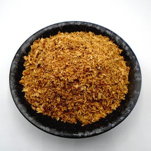 May include: A black bowl filled with a mound of dried, shredded, light brown ginger.