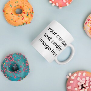 May include: White ceramic mug with the text "Your custom text and/or image here" on a light blue background with colourful doughnuts.