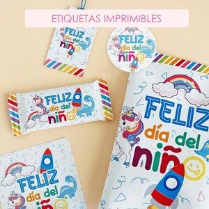 Puede incluir: Un conjunto de etiquetas y papel de regalo imprimibles con un diseño festivo. Los artículos presentan ilustraciones de unicornio, dinosaurio, cohete y arcoíris, con el texto "FELIZ día del niño" en azul y rojo. Las etiquetas tienen un fondo blanco con acentos coloridos.