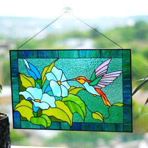 May include: A stained glass window panel depicting a hummingbird with outstretched wings, hovering near blue flowers with green leaves. The background is a teal blue.
