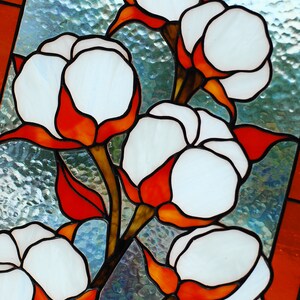 May include: Stained glass panel featuring cotton plants. The artwork showcases white cotton bolls with orange and red accents, set against a textured, light blue background. The panel is framed with an orange border.