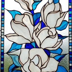 Puede incluir: Una ventana de vitrales que representa flores blancas con hojas azules y un borde azul.