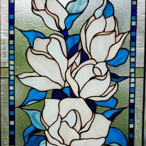 Puede incluir: Una ventana de vitrales que representa flores blancas de magnolia con hojas azules y un borde azul.