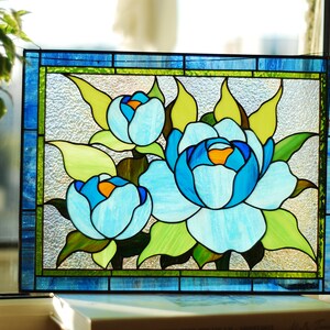 May include: A stained glass window panel depicting three blue flowers with green leaves. The flowers are surrounded by a blue and green border.