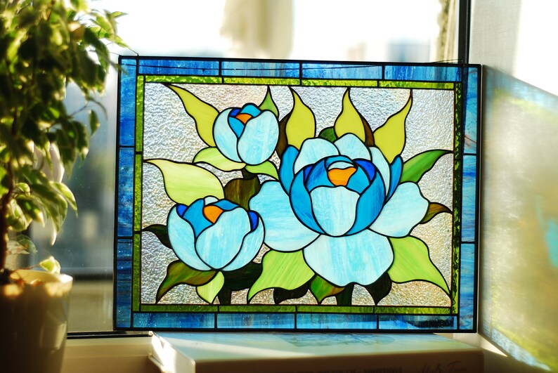 May include: A stained glass window panel depicting three blue flowers with green leaves. The flowers are surrounded by a blue and green border.