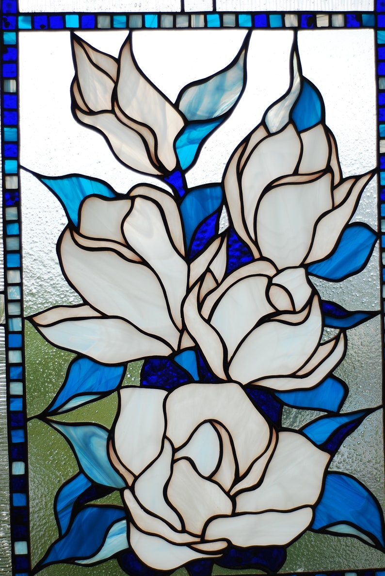 Puede incluir: Una ventana de vitrales que representa flores blancas de magnolia con hojas azules y verdes. Las flores est&aacute;n dispuestas en un racimo, con la flor m&aacute;s grande en el centro.