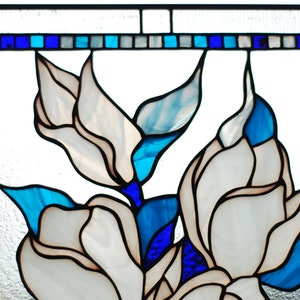 Puede incluir: Un panel de vitral con flores blancas y hojas azules y azul claro. Las flores son estilizadas y tienen una apariencia delicada, casi transl&uacute;cida.