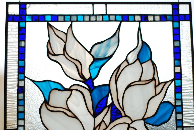Puede incluir: Un panel de vitral con flores blancas y hojas azules y azul claro. Las flores son estilizadas y tienen una apariencia delicada, casi transl&uacute;cida.