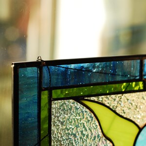 May include: A stained glass window panel with a floral design. The panel features blue, green, and yellow glass pieces. The glass is textured and has a frosted appearance.