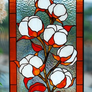 May include: Stained glass panel featuring a cotton plant design. The artwork showcases white cotton bolls with orange and red accents, set against a textured glass background. The panel is framed with an orange border.
