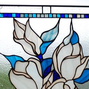 Puede incluir: Una ventana de vitrales que representa flores blancas con acentos azules y azul claro. Las flores est&aacute;n dispuestas en un racimo y est&aacute;n rodeadas por un borde azul oscuro.