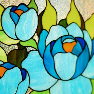 May include: Stained glass window featuring three blue flowers with orange centers. The flowers are surrounded by green leaves.