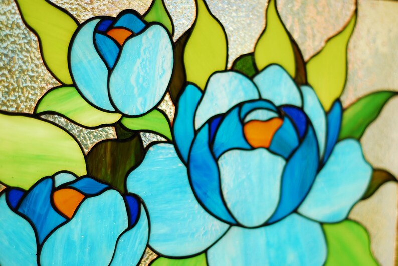 May include: Stained glass window featuring three blue flowers with orange centers. The flowers are surrounded by green leaves.