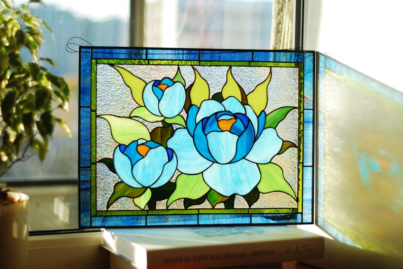 May include: A stained glass window panel depicting three blue peonies with green leaves. The panel is framed in blue and green glass.