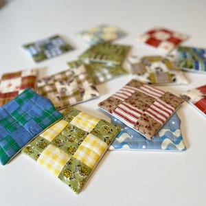 May include: A collection of 10 colorful quilted fabric squares with various patterns, including floral, plaid, and geometric designs. The squares are arranged in a random pattern on a white surface.