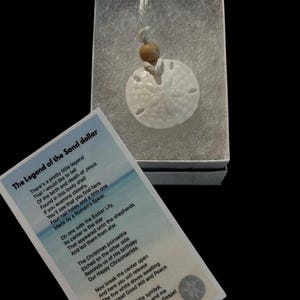 May include: A white sand dollar necklace with a brown wooden bead and a card that reads "The Legend of the Sand Dollar" with a poem about the religious significance of the sand dollar.