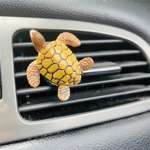 May include: A yellow and brown turtle car air freshener hanging from a car's air vent.