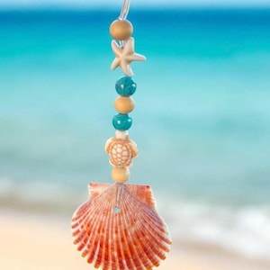 May include: A seashell charm with a beaded string featuring a starfish, a turtle, and turquoise beads. The charm is hanging from a clear string.