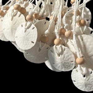 May include: A group of white sand dollar ornaments with a white string and wooden beads. The sand dollars are hanging from the string.