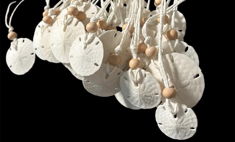 May include: A group of white sand dollar ornaments with a white string and wooden beads. The sand dollars are hanging from the string.