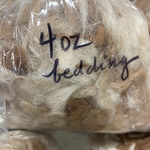 May include: A clear plastic bag filled with light brown bedding material. The bag is labeled with black marker, reading "4 oz bedding". The bedding appears to be soft and fluffy.
