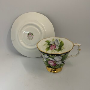 May include: A Royal Albert teacup and saucer with a black background and a floral design featuring pink and white flowers. The saucer has the Royal Albert logo on the bottom.