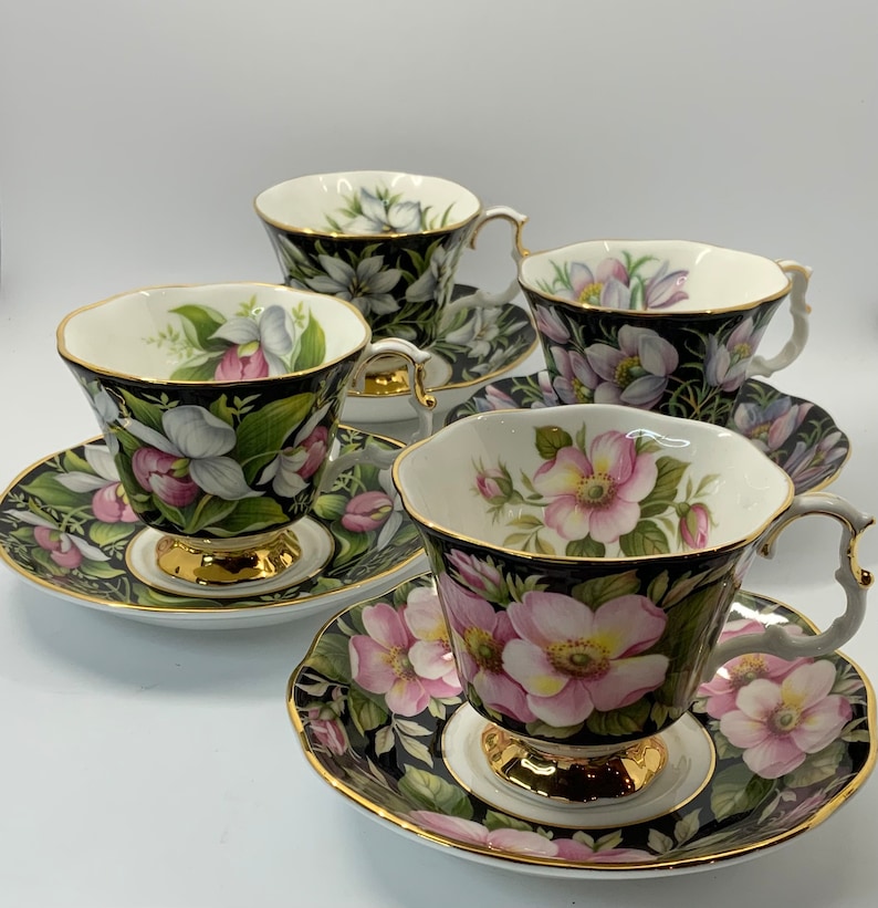 May include: Four teacups and saucers with floral patterns. The cups and saucers are white with gold trim. The floral patterns are in shades of pink, green, and white. The cups are all different, but they have a similar style.