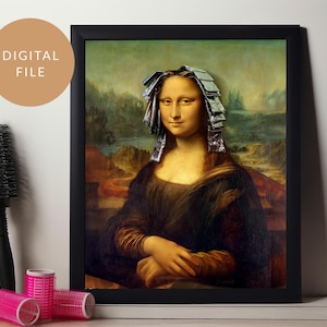 May include: A framed print of the Mona Lisa with foil highlights, a humorous take on a classic artwork. The image is surrounded by a black frame, with the words "DIGITAL FILE" in a tan circle. A black round brush and pink hair rollers are on the left.