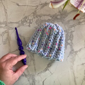 Può includere: Un cappello all'uncinetto blu chiaro con macchie colorate. Il cappello è realizzato con un filato morbido e soffice e ha una vestibilità morbida.