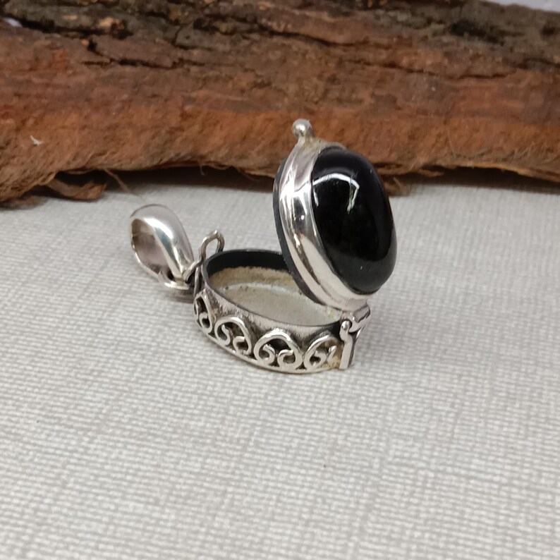 May include: A silver locket pendant with an oval black onyx stone. The locket is open and has a delicate filigree design.