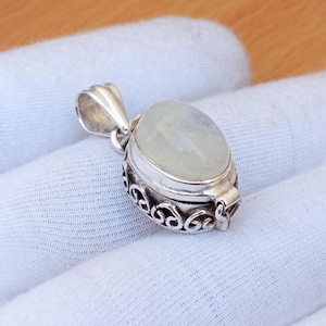 May include: A silver locket pendant with an oval-shaped white moonstone. The locket has a detailed, ornate design and a hinged opening.
